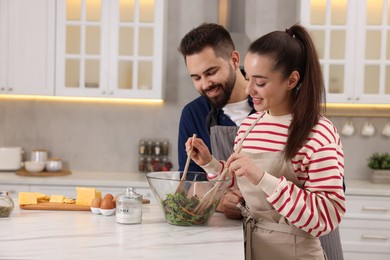 Photo of Happy affectionate couple cooking together at white table in kitchen