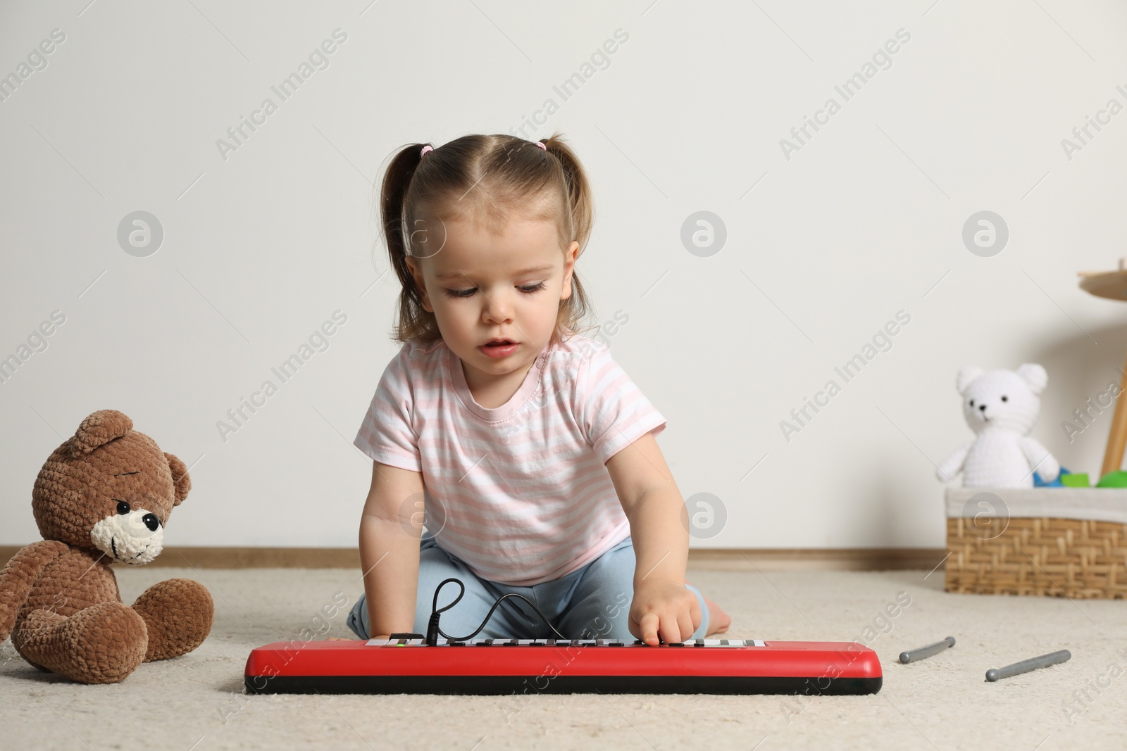 Photo of Cute little girl playing with toy piano at home