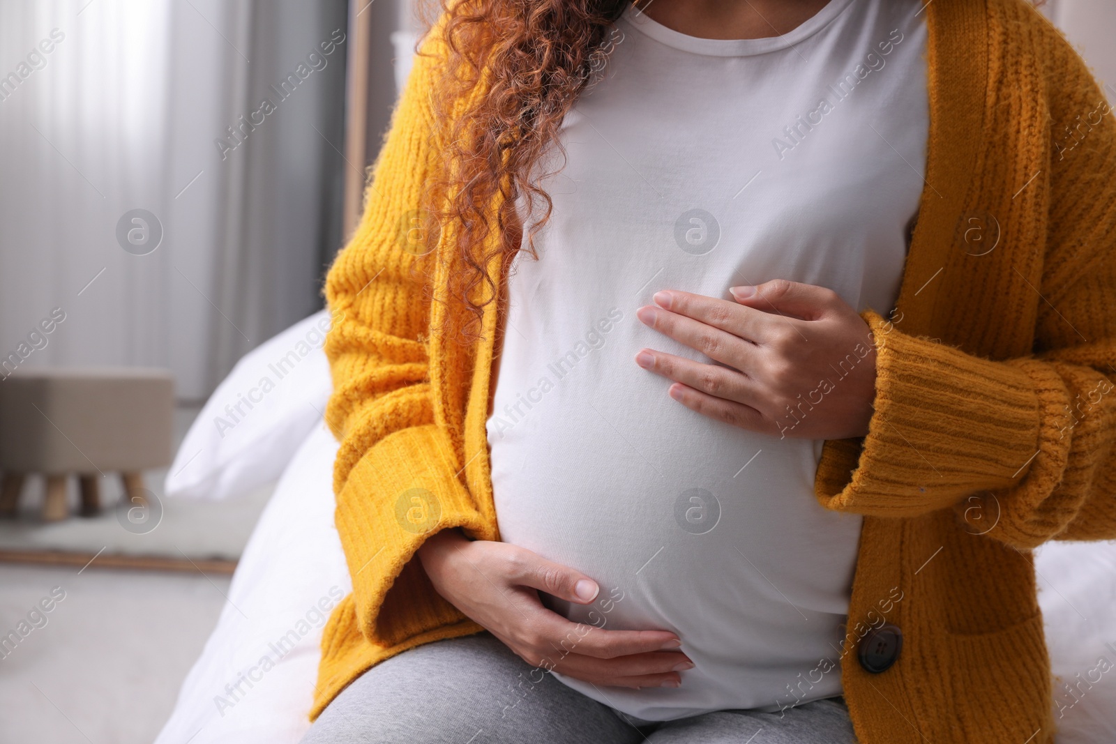 Photo of Pregnant African-American woman sitting on bed at home, closeup