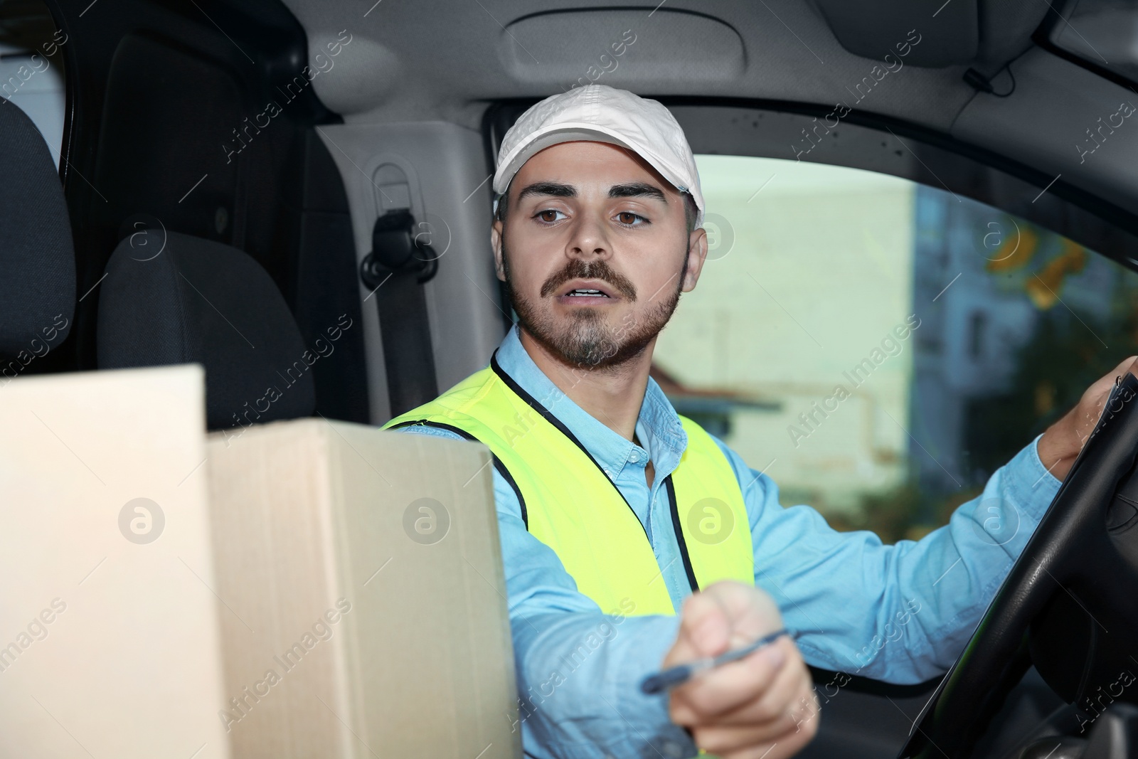 Photo of Young courier checking amount of parcels in delivery van