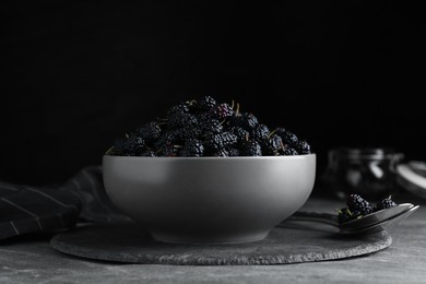Bowl of delicious ripe black mulberries on grey table