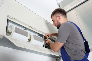 Photo of Young male technician repairing air conditioner indoors