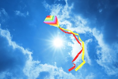 Image of Bright striped rainbow kite flying in blue sky on sunny day