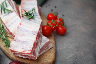 Raw pork ribs, rosemary and tomatoes on grey table, closeup. Space for text
