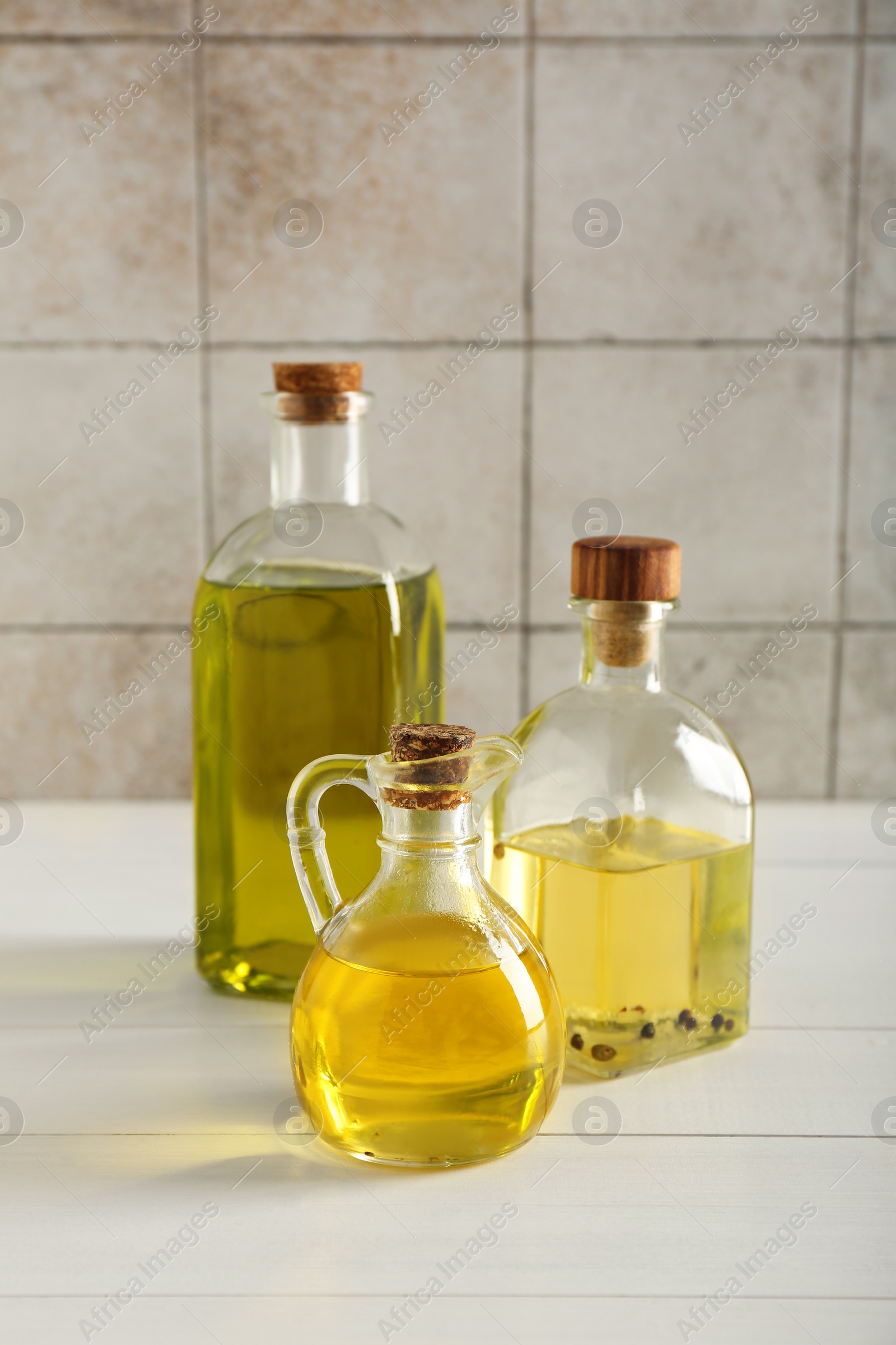 Photo of Vegetable fats. Different oils in glass bottles on white wooden table against tiled wall