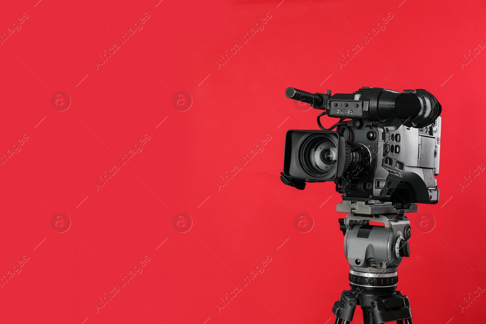 Photo of Modern professional video camera on red background. Space for text