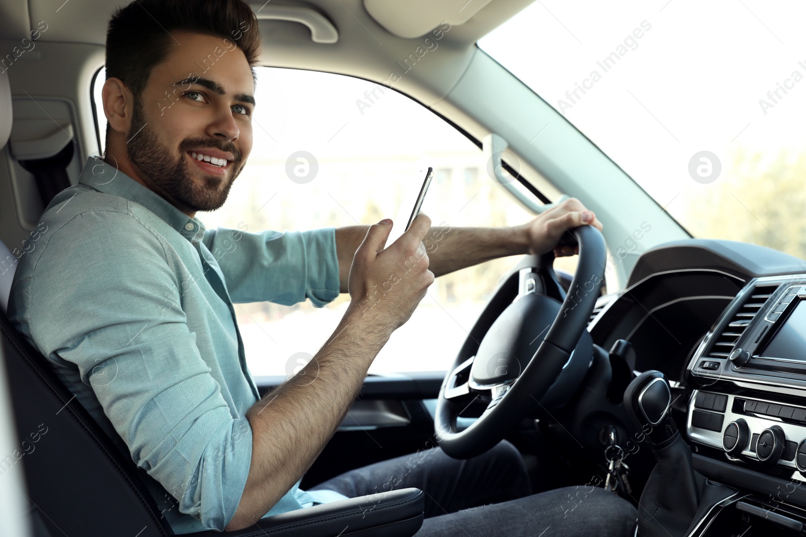 Photo of Handsome young man with smartphone driving his car