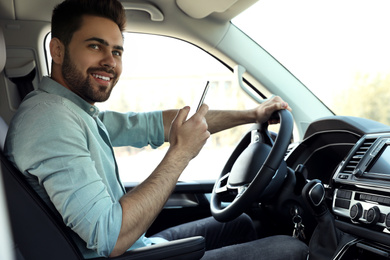 Photo of Handsome young man with smartphone driving his car
