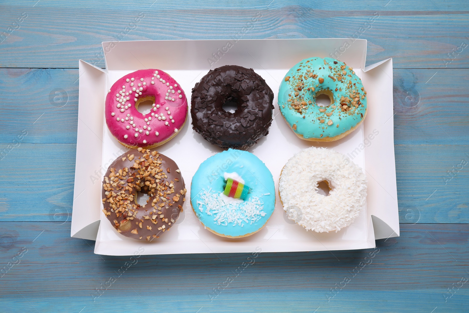 Photo of Box with different tasty glazed donuts on light blue wooden table, top view