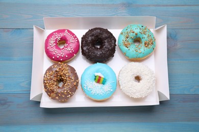 Box with different tasty glazed donuts on light blue wooden table, top view
