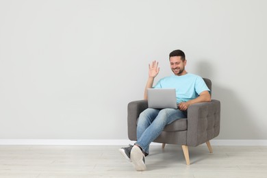 Happy man sitting in armchair and having video chat via laptop indoors, space for text