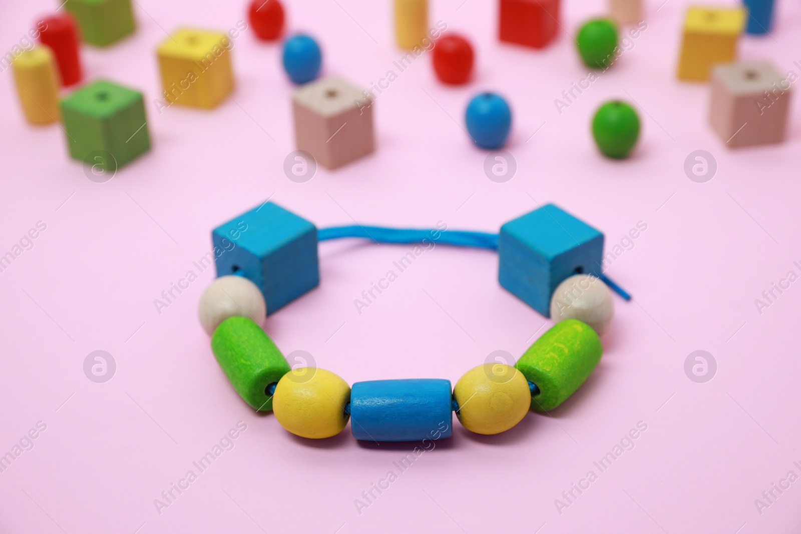 Photo of Wooden pieces and string for threading activity on pink background, closeup. Educational toy for motor skills development