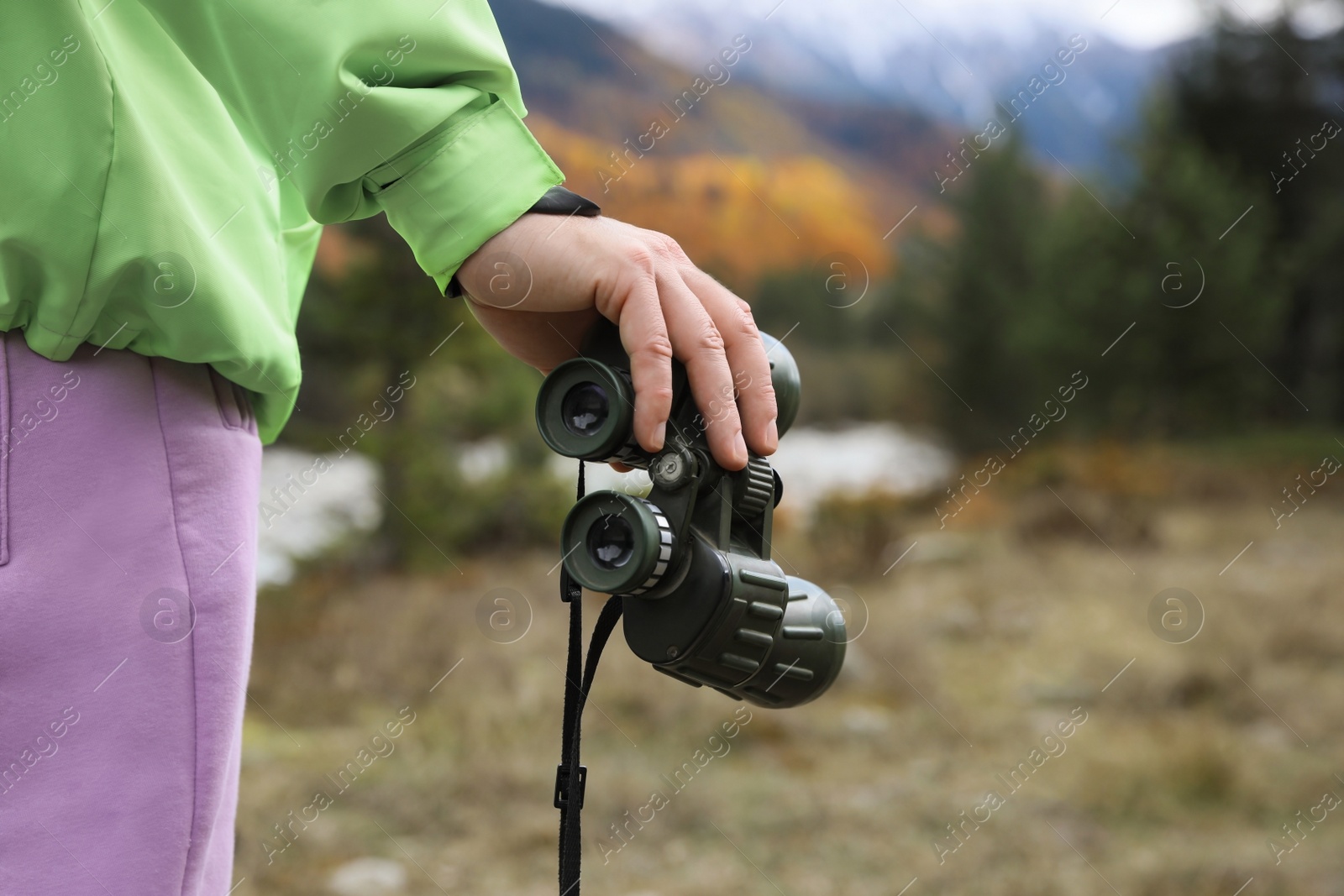 Photo of Woman holding binoculars in beautiful mountains, closeup. Space for text