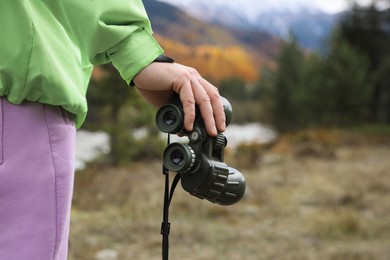 Photo of Woman holding binoculars in beautiful mountains, closeup. Space for text