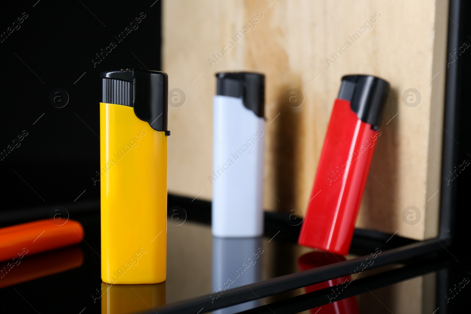 Photo of Stylish presentation of colorful plastic cigarette lighters standing on black and beige shelf