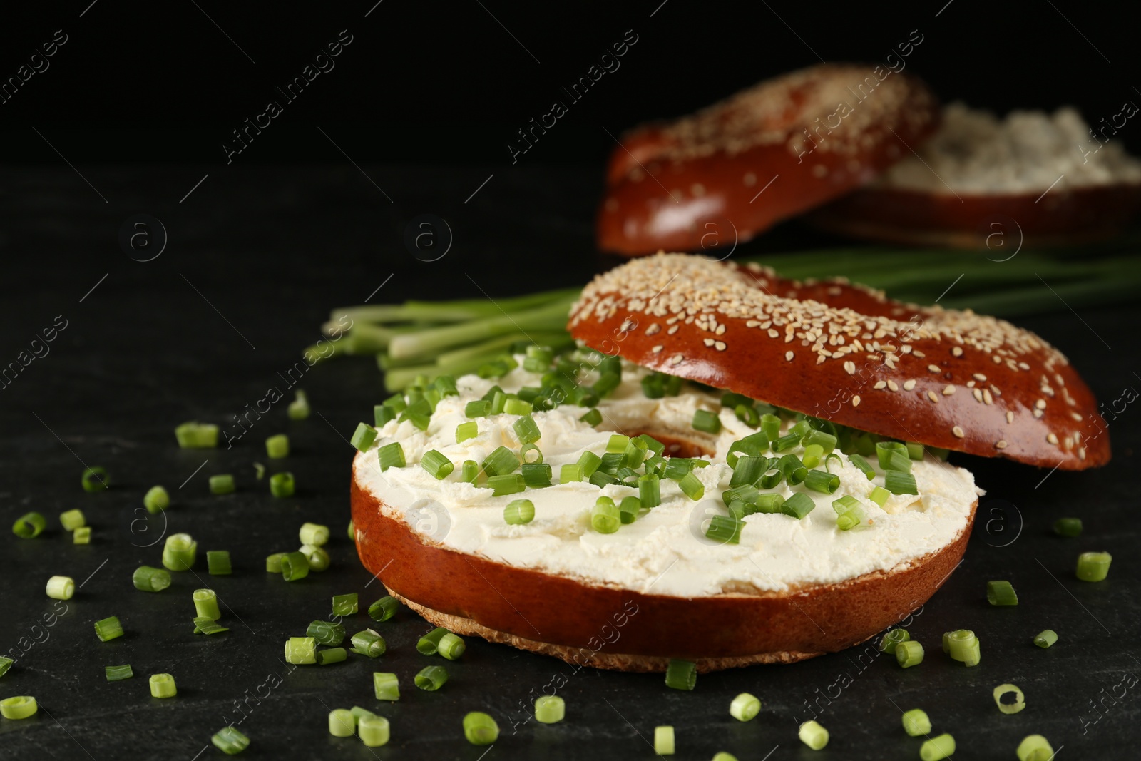 Photo of Delicious bagel with cream cheese and green onion on black table