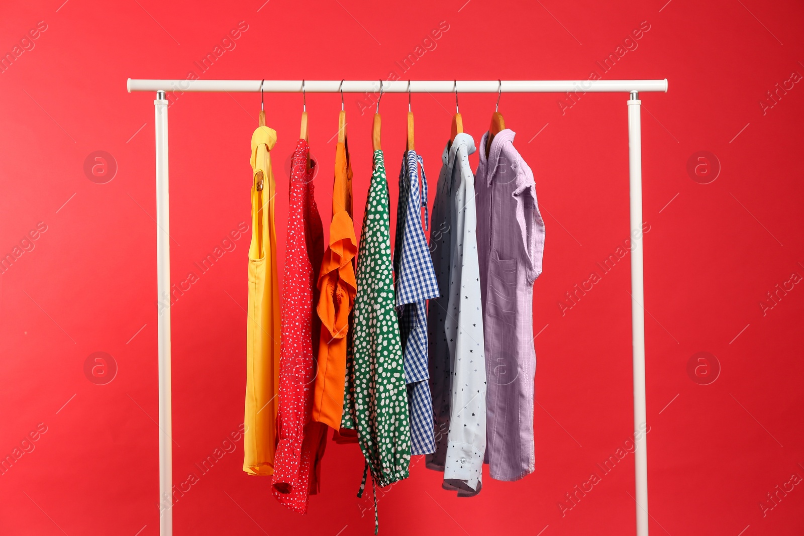 Photo of Bright clothes hanging on rack against red background. Rainbow colors