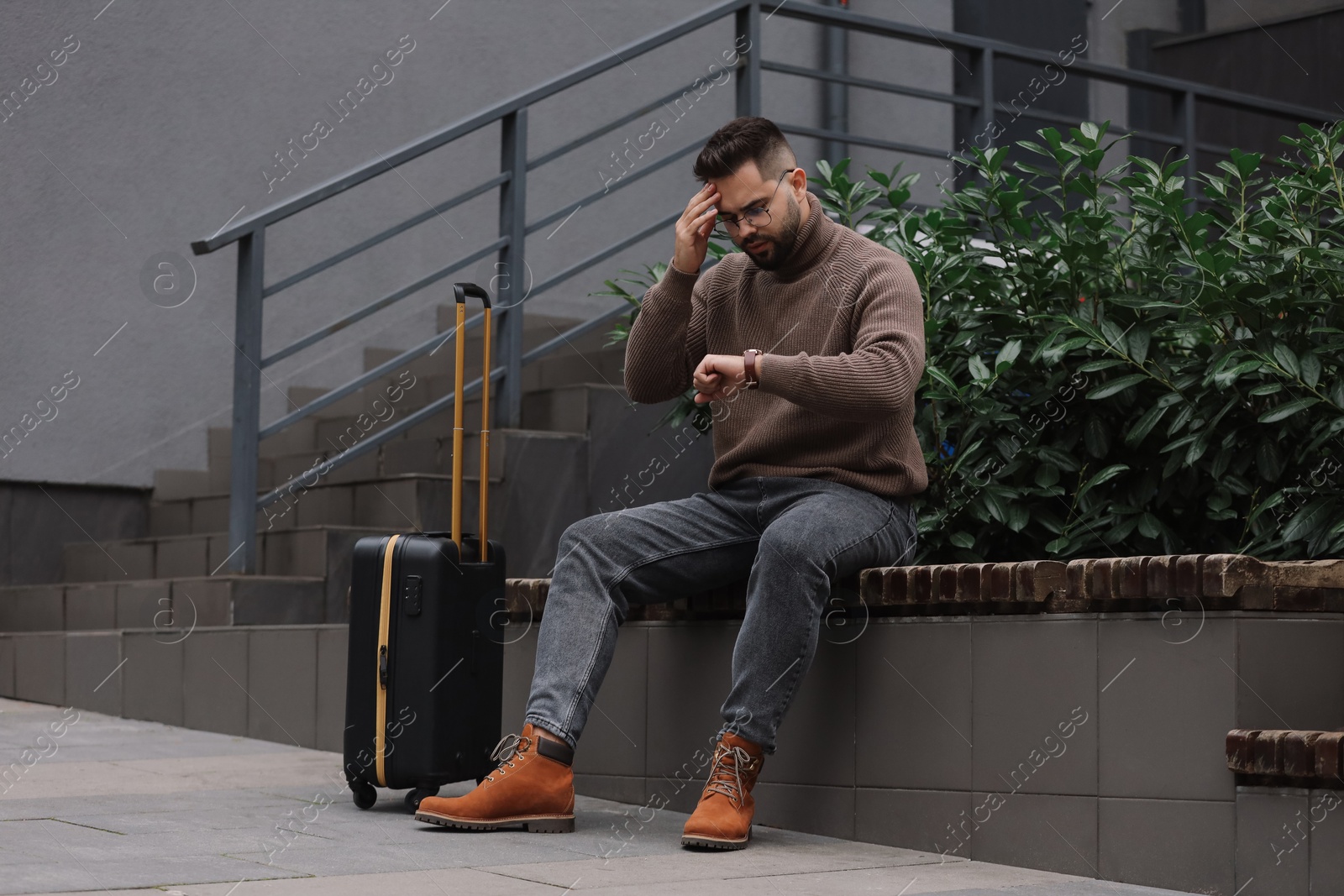 Photo of Being late. Worried man with suitcase looking at watch on bench outdoors