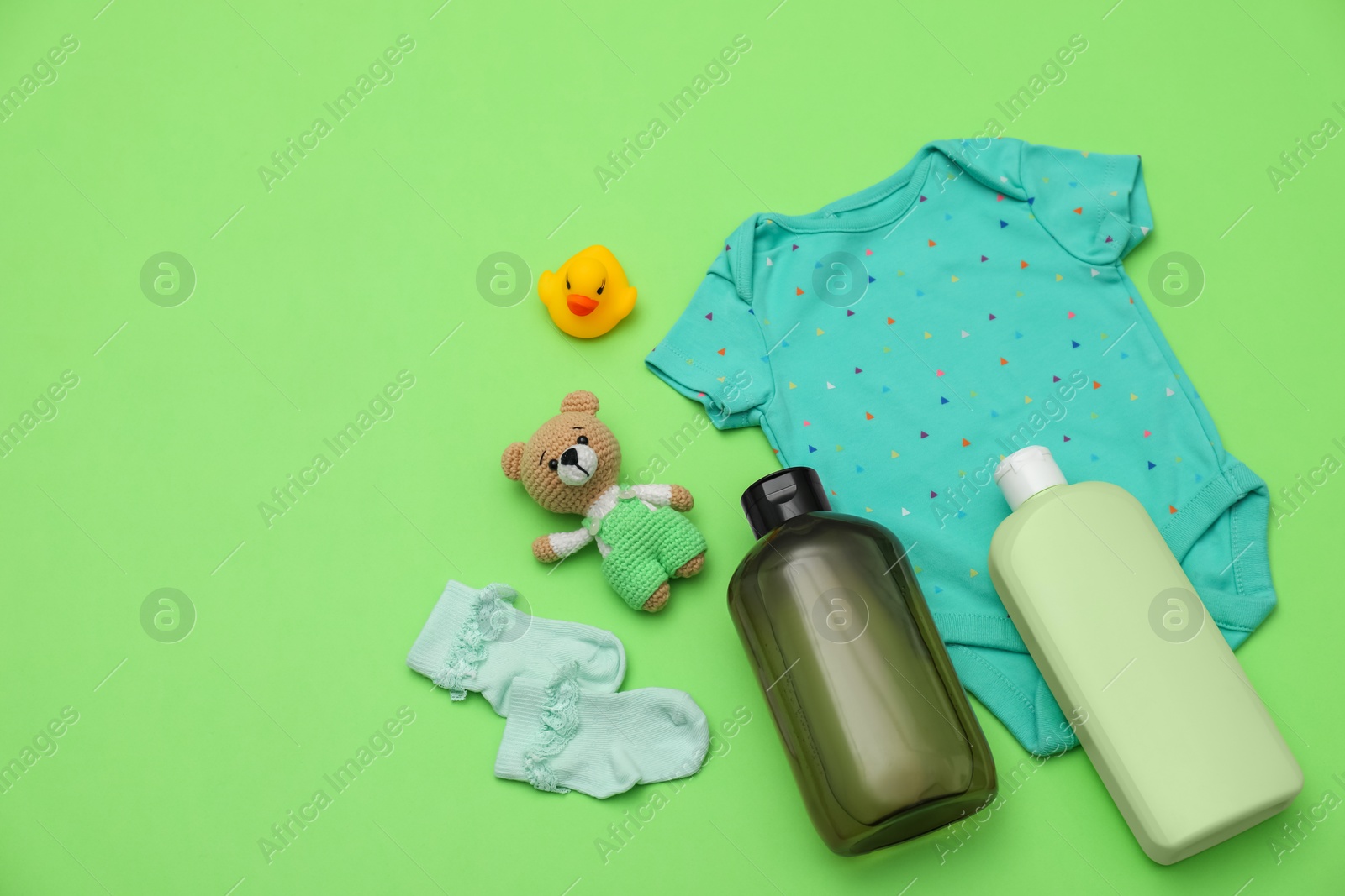 Photo of Bottles of laundry detergents, baby clothes and toys on light green background, flat lay. Space for text