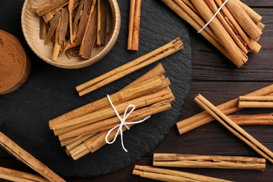 Photo of Aromatic cinnamon sticks and powder on wooden table, flat lay