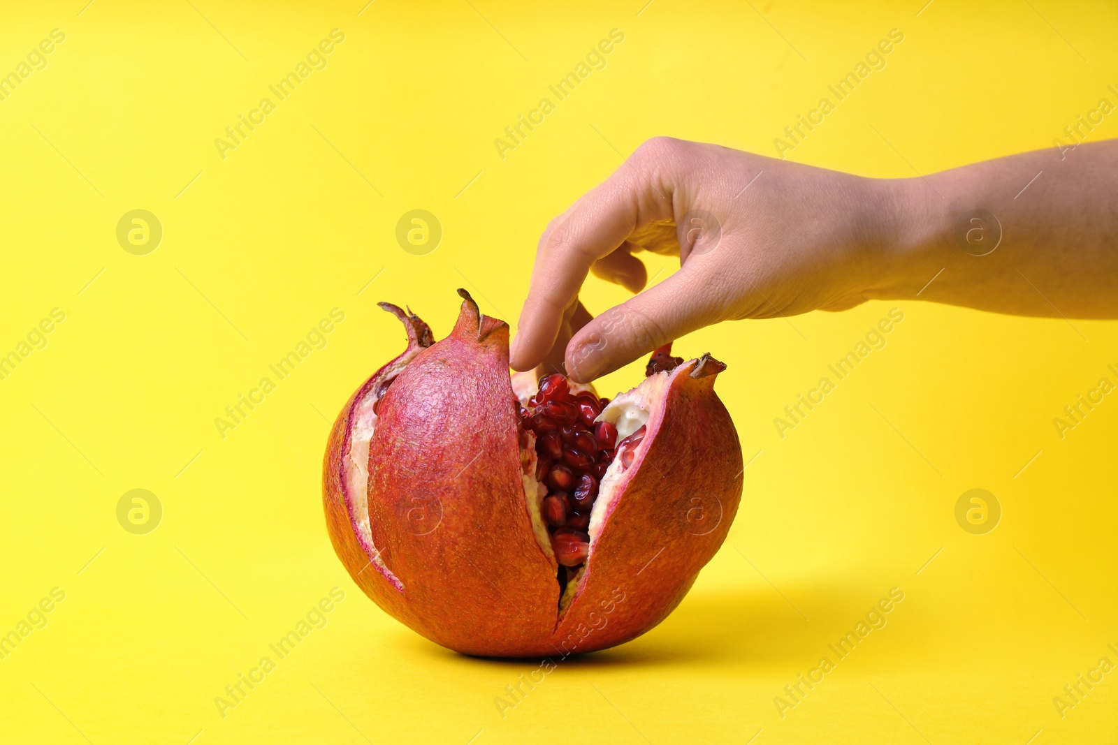 Photo of Woman taking pomegranate seeds from fruit on color background