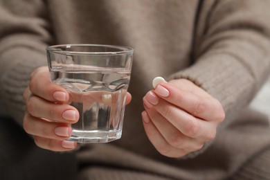 Photo of Woman holding glass of water and pill, closeup view