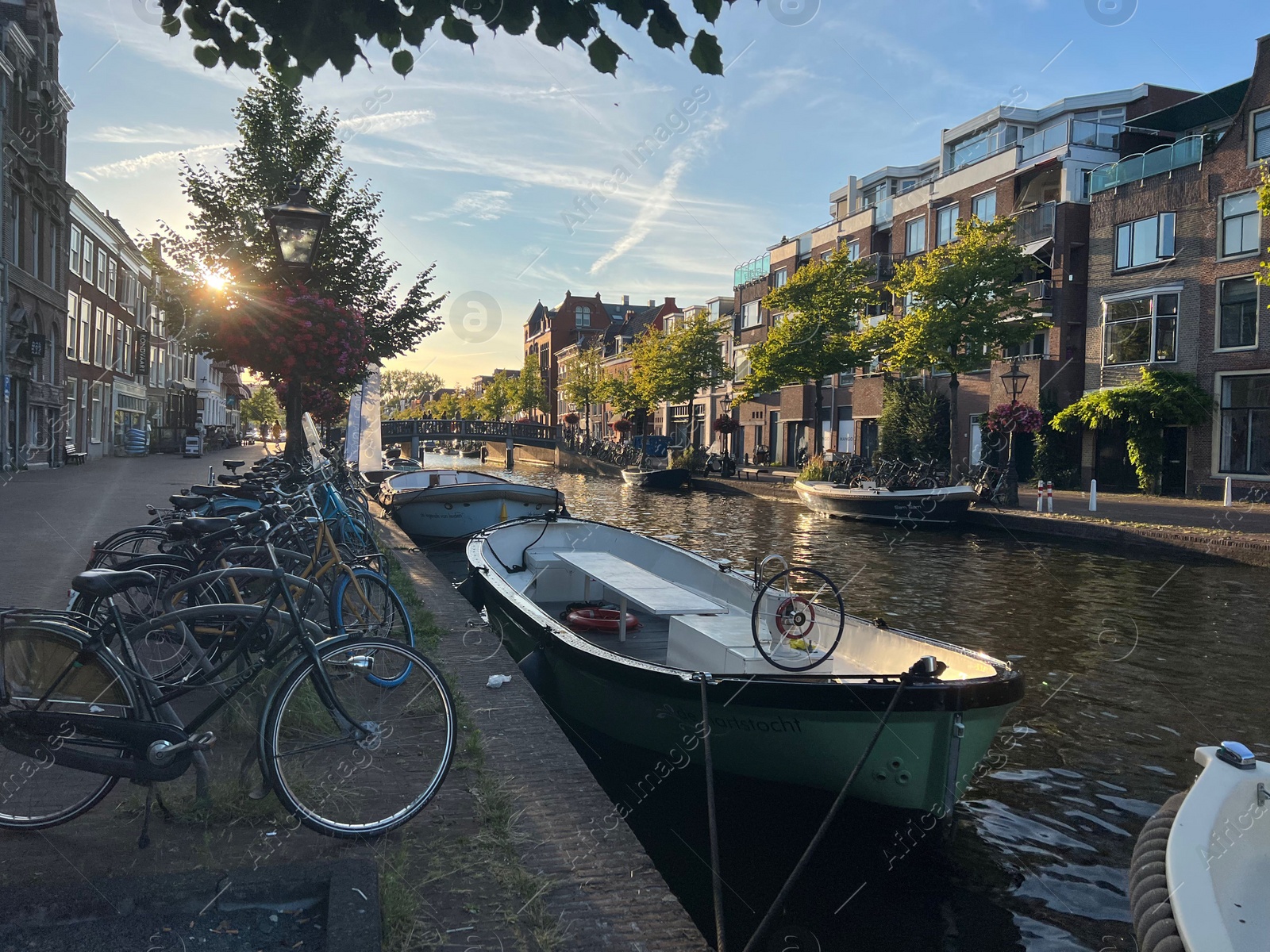 Photo of Leiden, Netherlands - August 1, 2022: Picturesque view of city canal with moored boats and parked bicycles