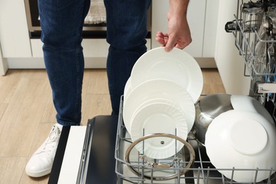 Photo of Man loading dishwasher with plates indoors, closeup