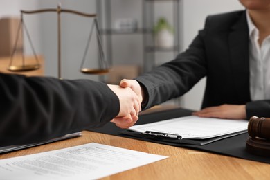 Photo of Notary shaking hands with client at wooden table in office, closeup