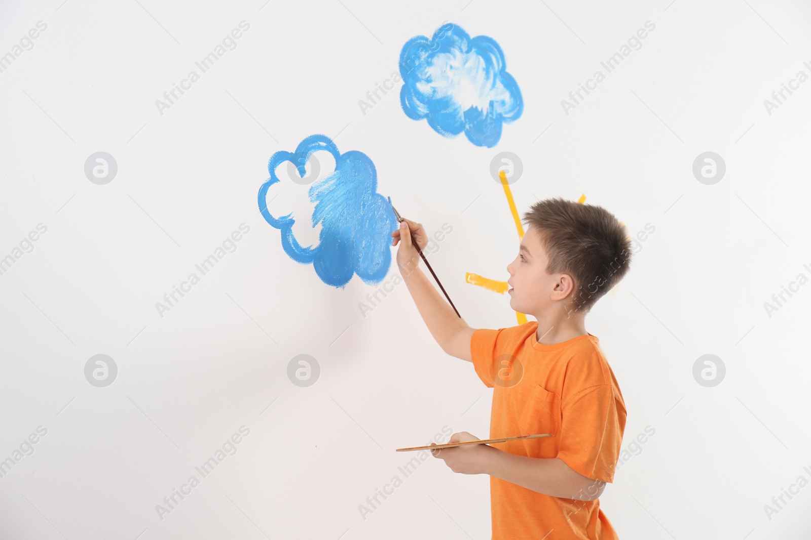 Photo of Little child painting cloud on white wall in room