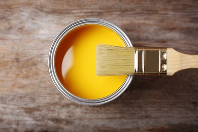 Photo of Can with yellow paint and brush on wooden background, top view