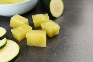 Photo of Frozen zucchini puree cubes and fresh zucchini on grey table. Space for text