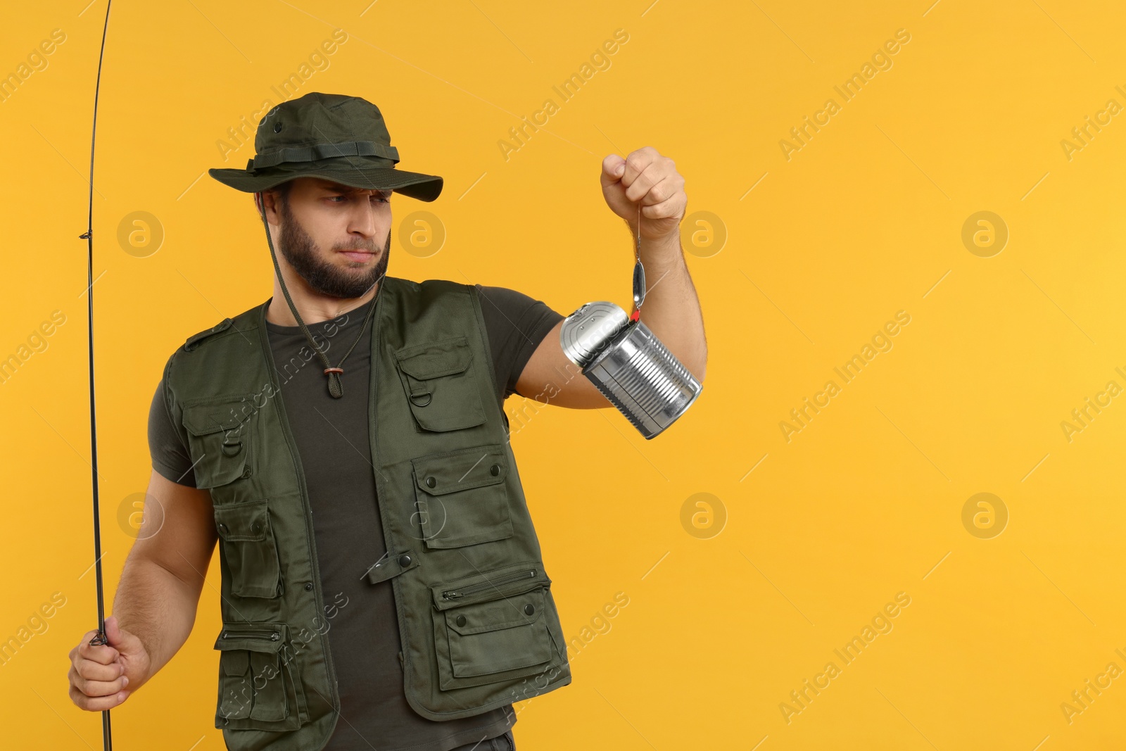 Photo of Fisherman holding rod and tin can on yellow background, space for text