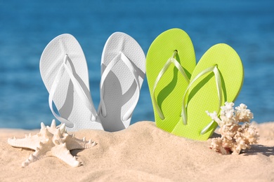 Photo of Composition with bright flip flops on sand near sea in summer. Beach accessories