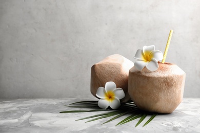 Photo of Young peeled coconuts with straw, palm leaf and beautiful flowers on grey table. Space for text