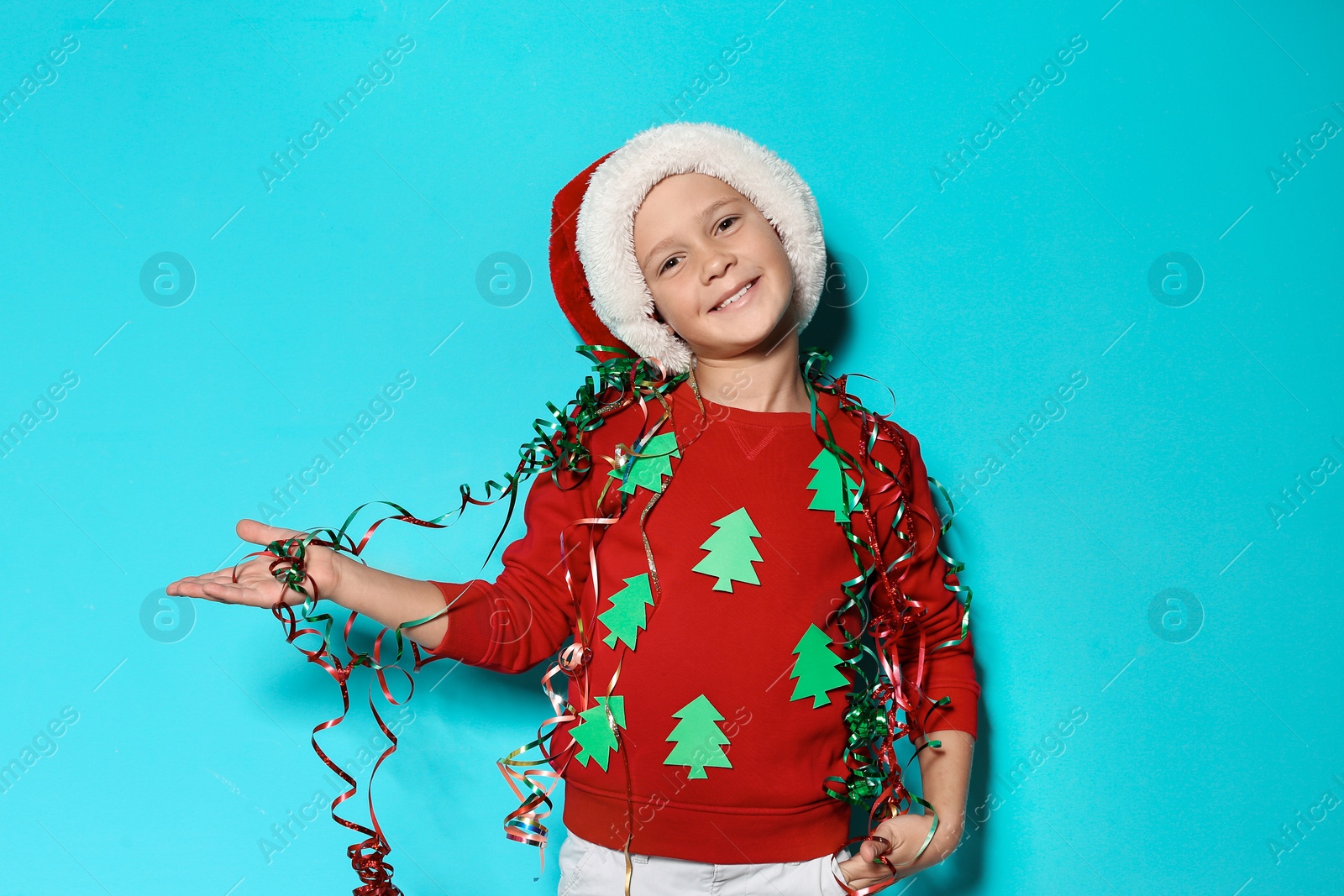 Photo of Cute little boy in handmade Christmas sweater and hat with streamers on color background