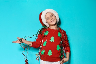 Cute little boy in handmade Christmas sweater and hat with streamers on color background
