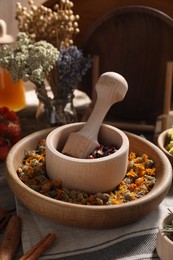 Mortar with pestle, many different dry herbs and flowers on table