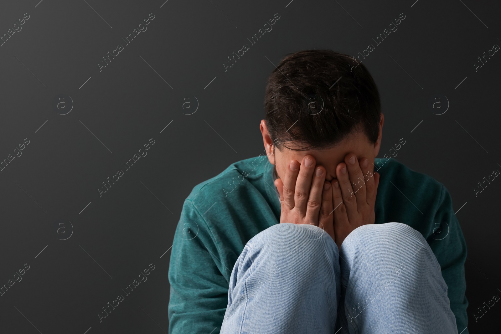 Photo of Upset man sitting on black background. Space for text