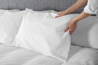 Photo of Woman fluffing soft pillow in bedroom, closeup