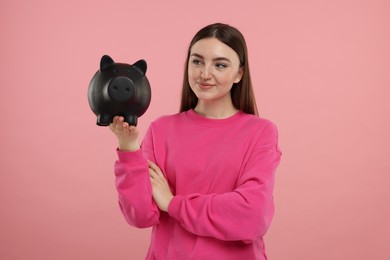 Happy woman with piggy bank on pink background