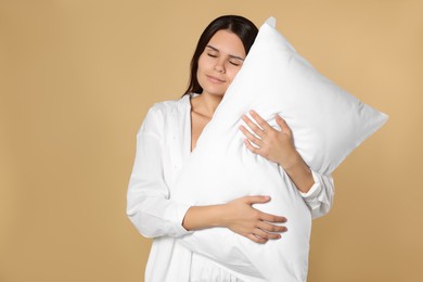 Sleepy young woman hugging soft pillow on beige background