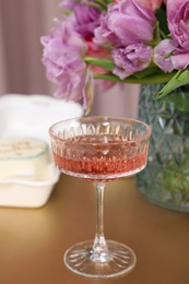 Photo of Glass of delicious wine and flowers on wooden table indoors, closeup