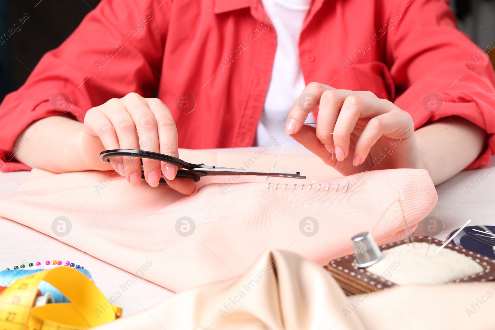 Photo of Woman cutting sewing thread over cloth at table, closeup