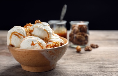 Photo of Tasty ice cream with caramel sauce and popcorn in bowl on wooden table