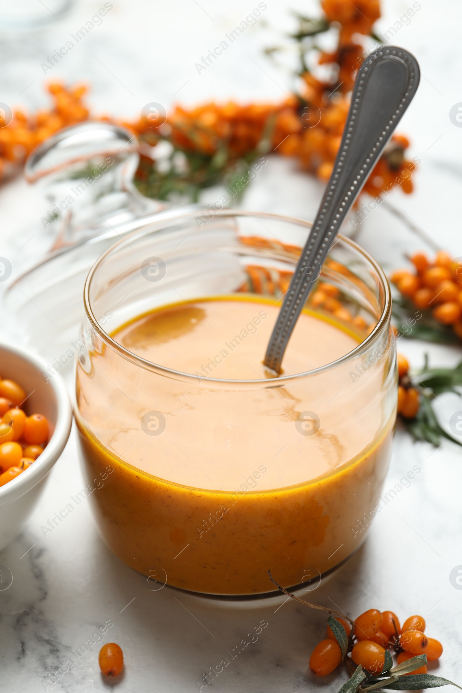 Photo of Delicious sea buckthorn jam and fresh berries on white marble table, closeup