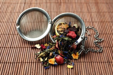 Photo of Snap infuser with dried herbal tea leaves and fruits on bamboo mat, closeup