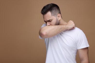 Photo of Sick man coughing on brown background, space for text