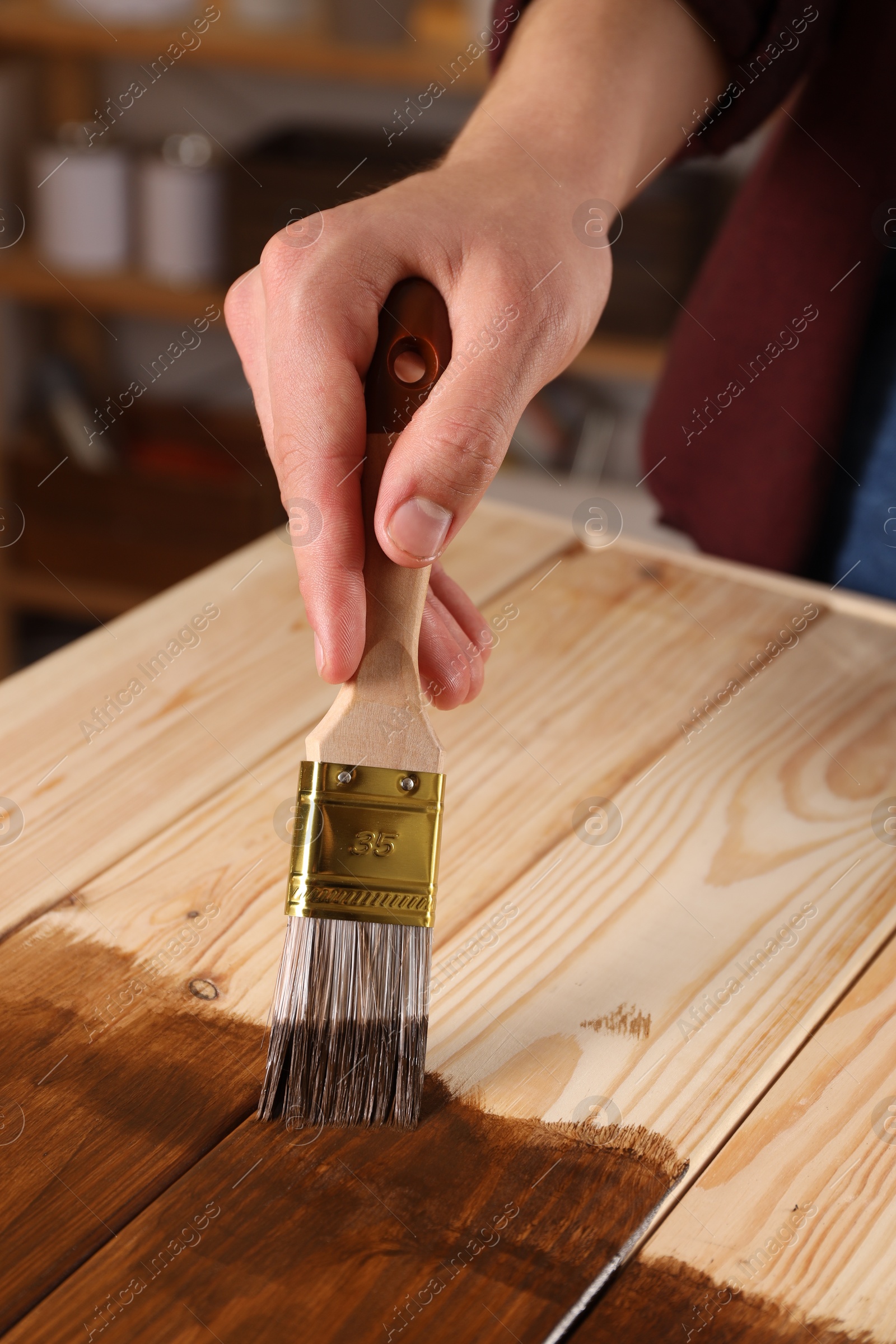 Photo of Man with brush applying wood stain onto wooden surface indoors, closeup