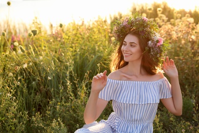 Photo of Young woman wearing wreath made of beautiful flowers outdoors on sunny day